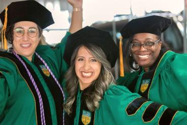 Three people wearing graduation regalia pose and smile for the camera