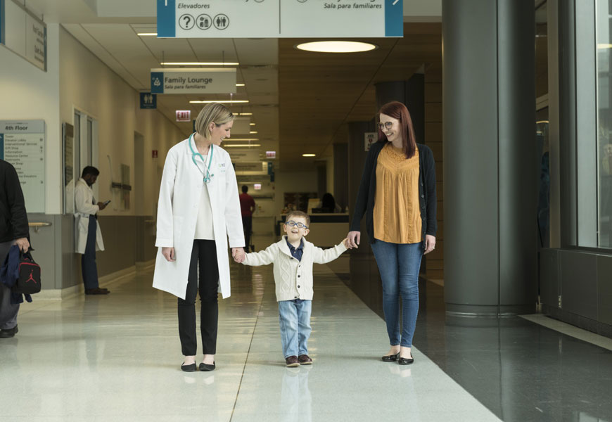 Young boy smiling walks holding hands with mother and doctor 
