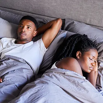 Man awake in bed next to a woman