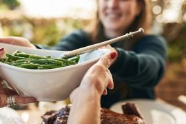 One Woman Passing a Bowl of Green Beans to Another Woman Across the Holiday Table