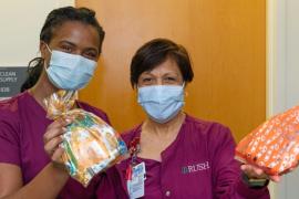 Two health care workers in scrubs and masks hold up colorful care packages