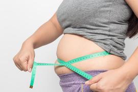 A woman measures her waist with a green measuring tape.