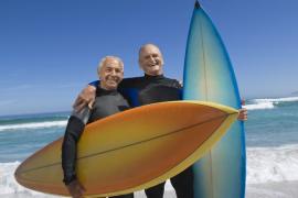 Two older men in wetsuits holding surfboards