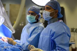 Dr. Parik Sharma performs a pacemaker implantation procedure in scrubs and a mask alongside another electrophysiologist.