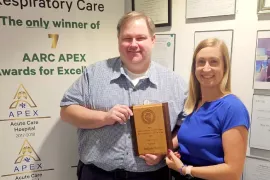 Two people stand together holding an award plaque