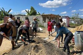 Students from the RISE program shovel dirt in front of a home in the Dominican Republic on a sunny day.