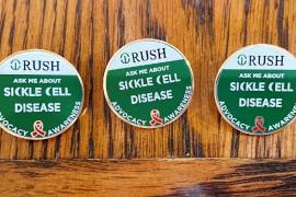 A row of enamel pins that say Ask Me About Sickle Cell Disease with the Rush logo
