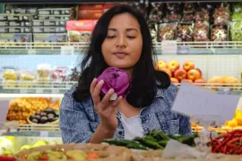 A young woman considers a vegetable she has picked out in the produce aisle of a grocery store.