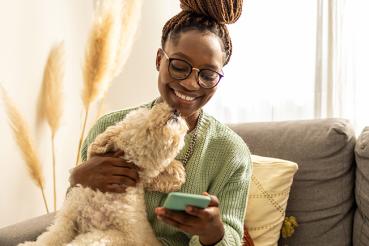 Woman being licked by her dog while she smiles at her cellphone