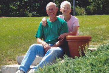 Mark, in green, and Anne, in pink sit in a grassy yard.