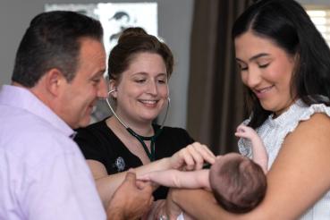 A mother and father hold a baby while a nurse uses a stethoscope to listen to the baby's heart