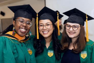 Three people wearing graduation regalia pose and smile for the camera