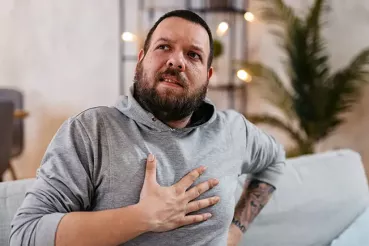 Man in gray shirt clutching chest