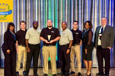 A group of students and faculty members standing on a stage holding an award