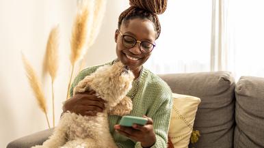 Woman being licked by her dog while she smiles at her cellphone