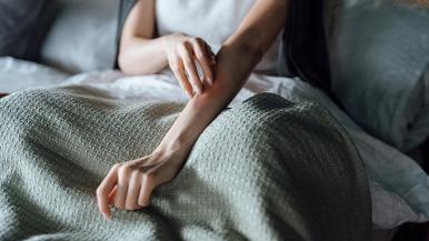 A woman scratching her arm in bed.