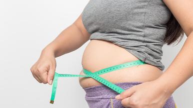 A woman measures her waist with a green measuring tape.