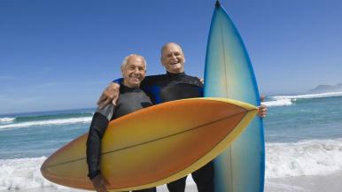 Two older men in wetsuits holding surfboards