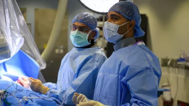 Dr. Parik Sharma performs a pacemaker implantation procedure in scrubs and a mask alongside another electrophysiologist.