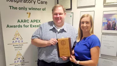 Two people stand together holding an award plaque