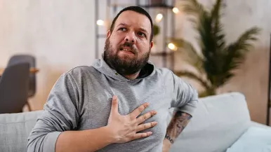 Man in gray shirt clutching chest