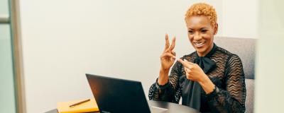A woman uses sign language facing a laptop. Photo credit Disability:IN