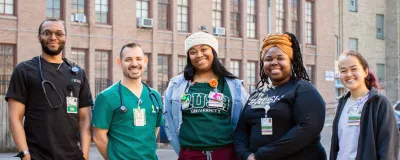 Group photo of five people standing together outside and smiling